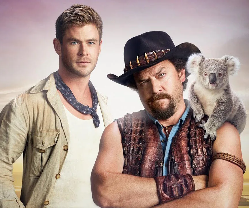 Two men in outback attire, one with a koala on his shoulder, posing against an outdoor background.