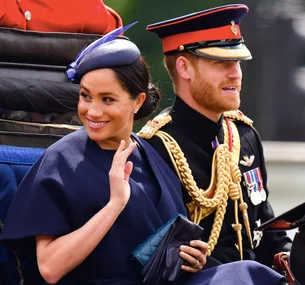 A woman waves from a carriage beside a man in a military uniform during a formal event.