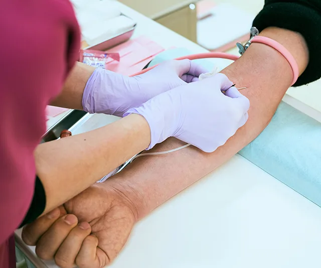 "Blood donation in progress with a medical professional inserting a needle into a donor's arm."