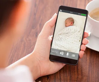 Person viewing a baby monitor app on a smartphone, showing a sleeping baby wrapped in a blanket.