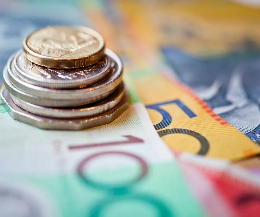 Stack of Australian coins on blurry colorful banknotes background.