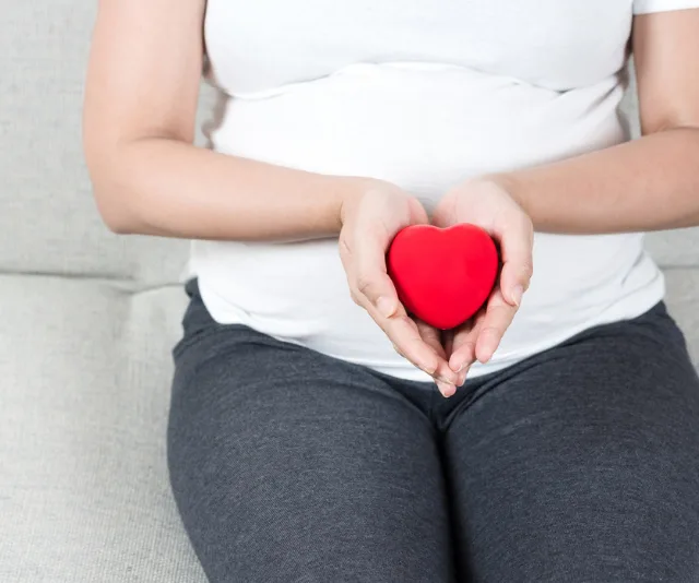 Pregnant woman holding a red heart-shaped object, symbolizing heart health during pregnancy.