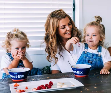 A mother with two children enjoying breakfast with Weet-Bix cereal at a table.