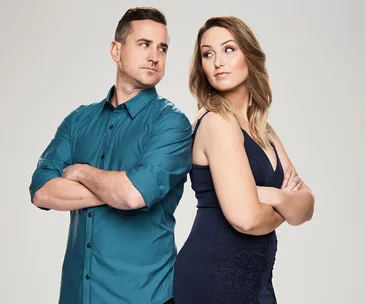 Two people stand back-to-back with arms crossed, looking at each other with playful expressions.