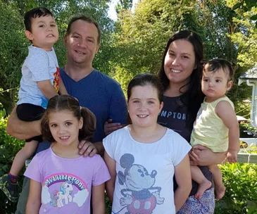 A family of six posing outdoors with trees in the background, including two adults and four children.
