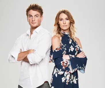 Man in white shirt and woman in floral dress stand with arms crossed against a gray background.