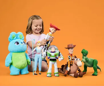 A child smiling, playing with Toy Story character dolls against an orange background, including Woody and Buzz Lightyear.