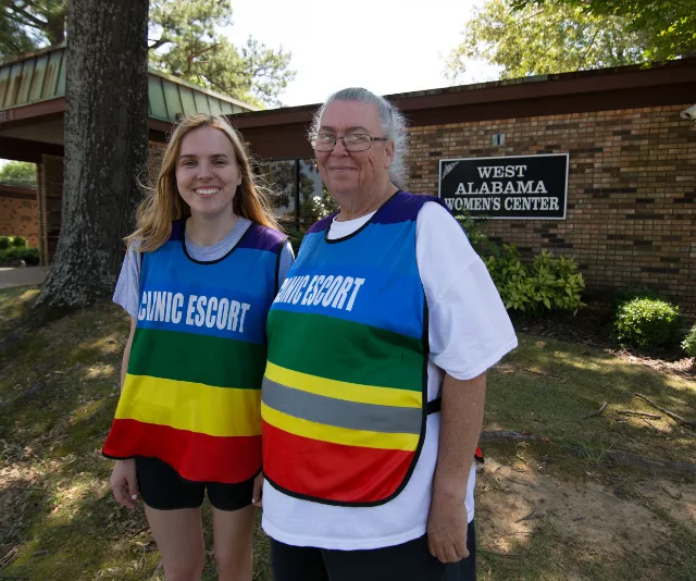 Clinic escorts in colorful vests stand outside West Alabama Women's Center building.