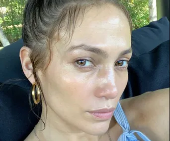 A woman with hoop earrings and a striped top sitting outdoors, looking at the camera with a serious expression.