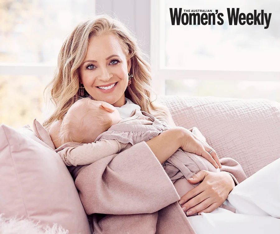 Woman smiling, holding a baby while sitting on a couch; "The Australian Women's Weekly" logo in the corner.