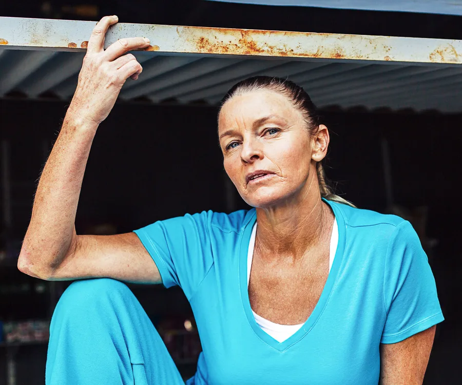 Woman in blue shirt sitting under a metal structure, looking serious.