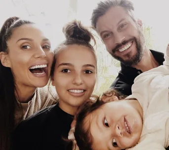 A happy family of four smiling for a selfie, with two adults and two children close together.