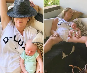 Woman napping on couch with baby, wearing a "D-LUXE" shirt and hat, baby in green onesie.