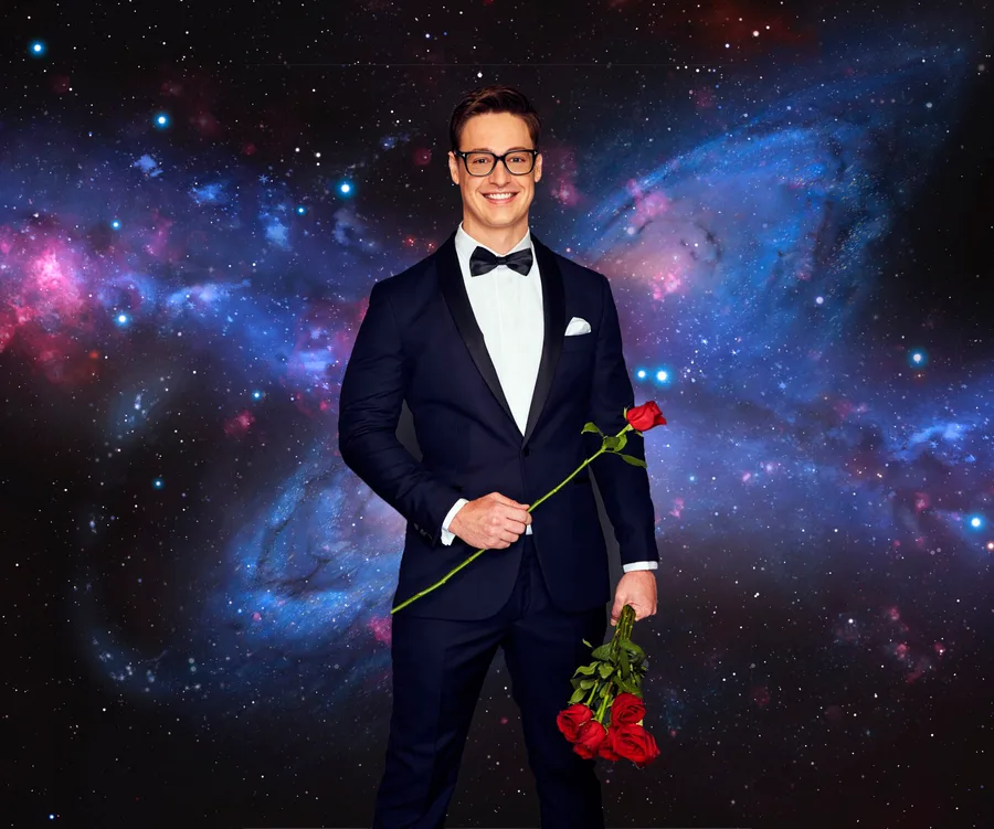Man in tuxedo holding roses, standing against a cosmic, star-filled background.