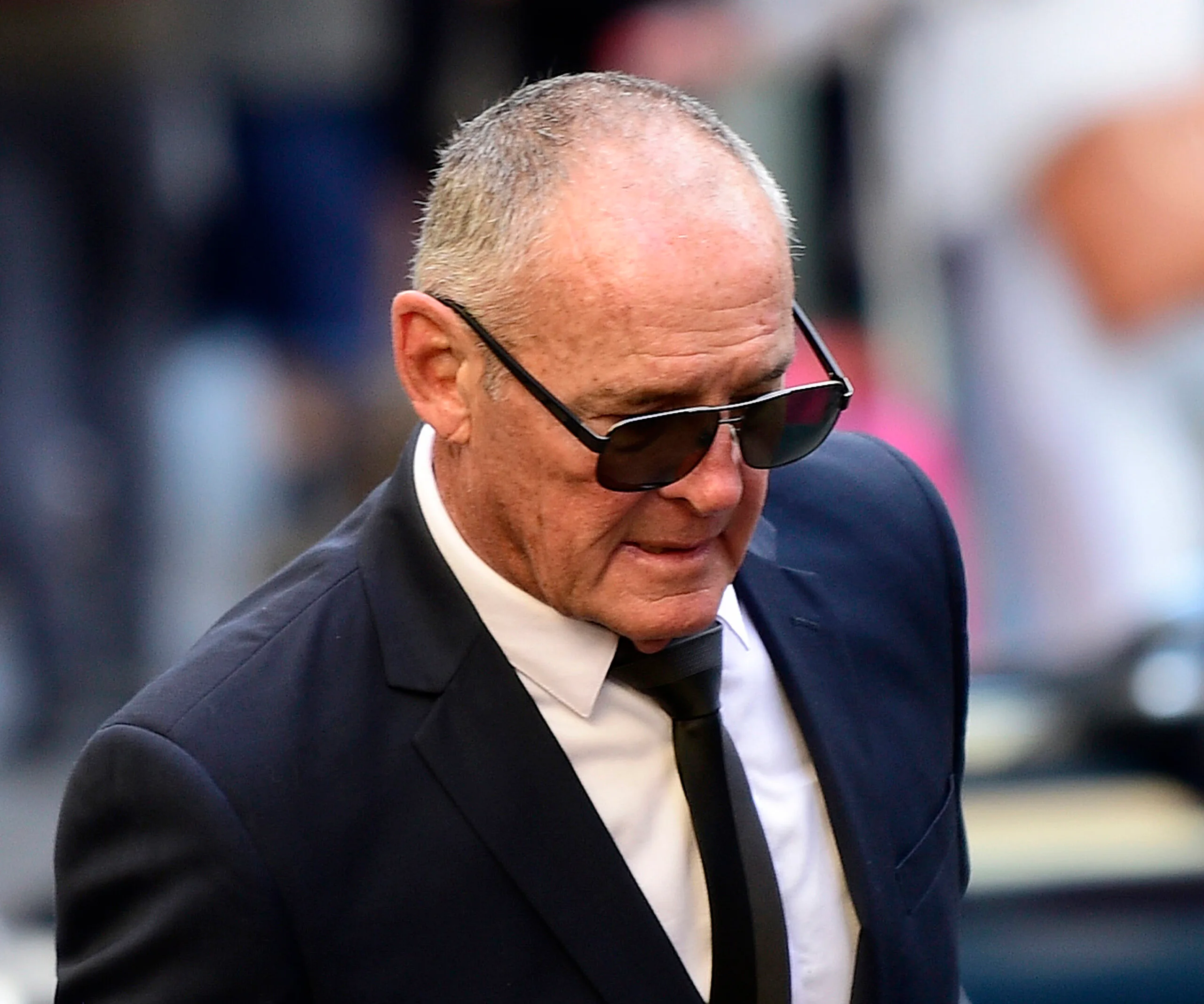 Man in sunglasses and suit, walking outdoors.