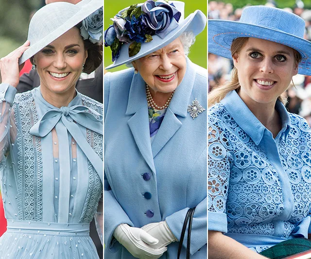 Women in elegant blue outfits and hats at a formal event, smiling.