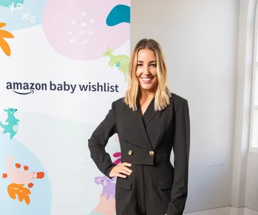 Person in black outfit smiling at Amazon Baby Wishlist event backdrop.
