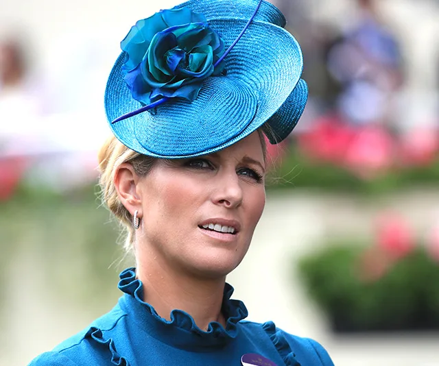 A woman in a blue dress and matching hat with a floral design at a formal outdoor event.