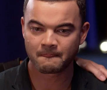 Man with short hair and beard, emotional, with a tear on his cheek, in a dimly lit setting.