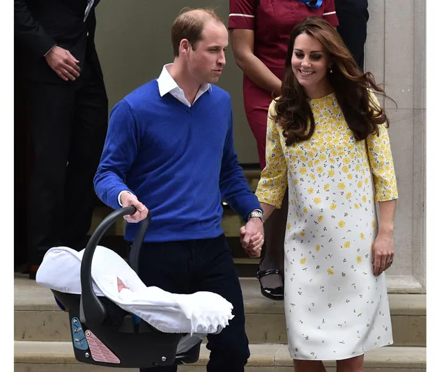 Couple walking out of a building, holding hands, with one carrying a baby in a car seat.