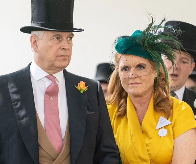 A man in a black top hat and morning suit with a woman in a green fascinator and yellow outfit at a formal event.