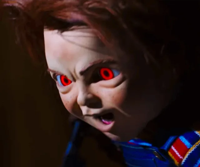 Close-up of Chucky, the doll, with glowing red eyes and an aggressive expression from "Child's Play" (2019).