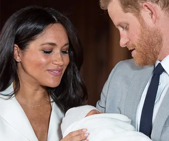 Couple holding a newborn wrapped in a white blanket, both gazing lovingly at the baby.