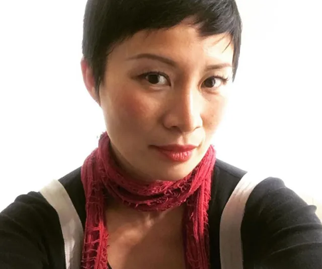 A woman with short black hair wearing a red scarf and black top, looking at the camera against a light background.
