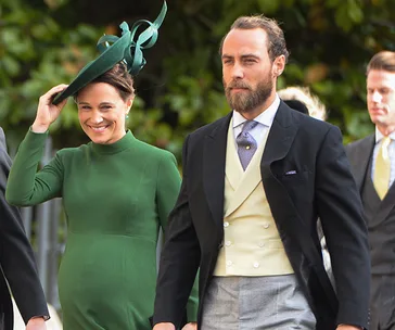 A woman in a green dress and hat walks with a man in formal attire at an outdoor event.