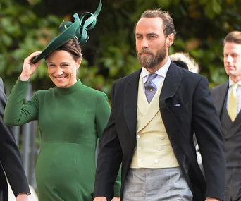 A woman in a green dress and hat walks with a man in formal attire at an outdoor event.