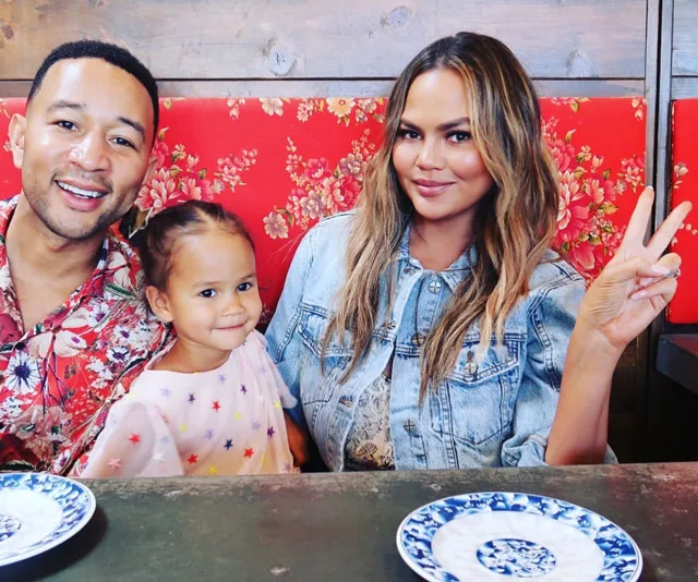 A family sitting at a table with floral background, woman showing peace sign, two plates visible.
