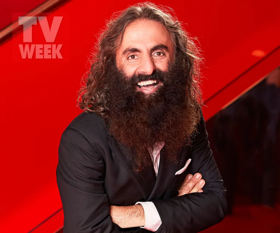 Man with long hair and beard in a suit, smiling against a vibrant red background with "TV WEEK" logo.