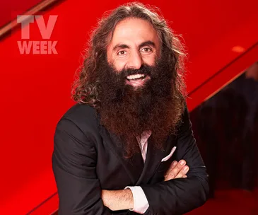 Man with long hair and beard in a suit, smiling against a vibrant red background with "TV WEEK" logo.