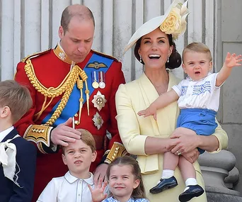 A family stands on a balcony; a man in uniform, woman in yellow and hat holding a child, other children in front.