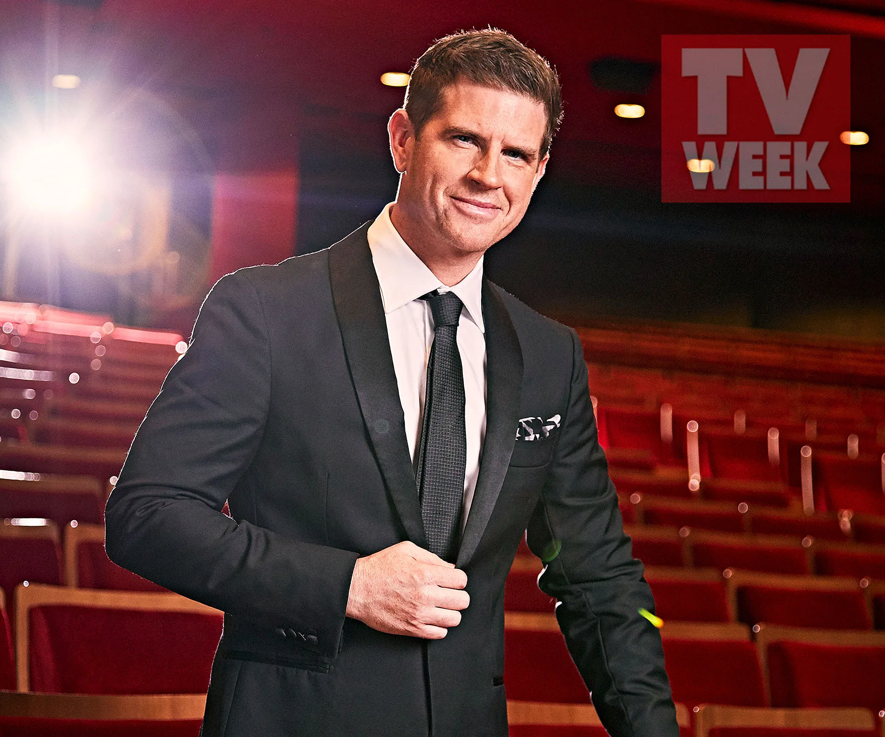 Man in a suit standing in an empty theater, lit from behind, with "TV WEEK" logo in the corner.