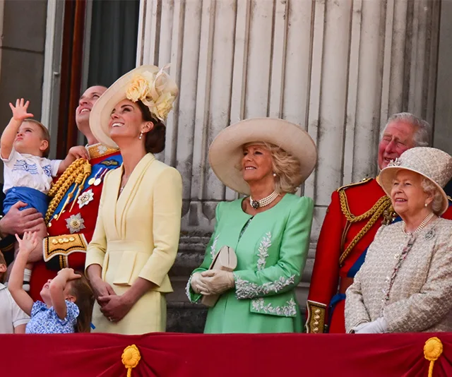 A group of elegantly dressed people on a balcony, looking up at an event in the sky.