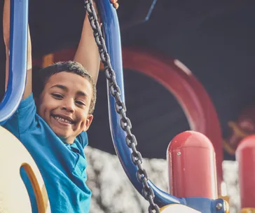 A child smiling while playing on blue monkey bars at a playground.