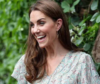 A woman smiling outdoors in a patterned dress with leafy background.