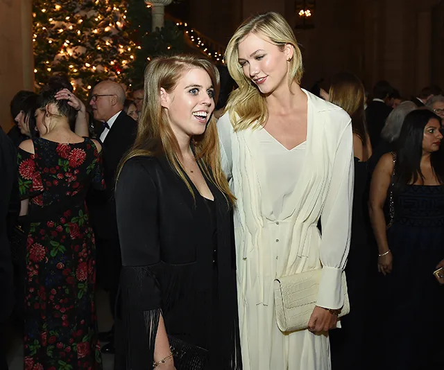 Two women in elegant attire smiling at a formal event with a decorated tree in the background.