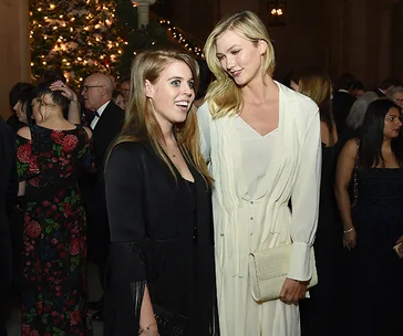 Two women in elegant attire smiling at a formal event with a decorated tree in the background.