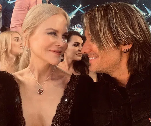 A couple smiling at each other in an audience setting, surrounded by other people.