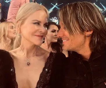A couple smiling at each other in an audience setting, surrounded by other people.