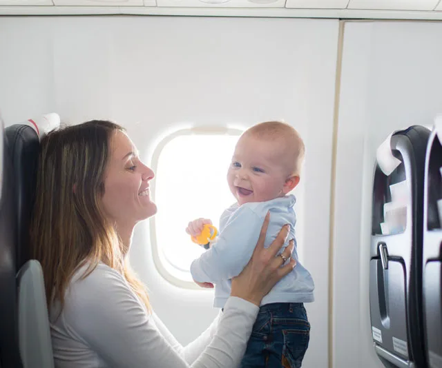 Woman holding and smiling at a baby by an airplane window.