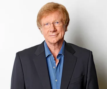 Man in a suit with glasses and light hair, against a plain background.