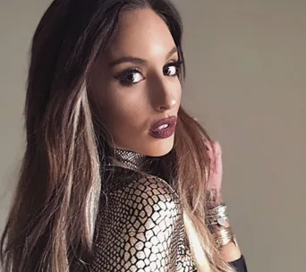 Woman with long hair and patterned top, looking over shoulder.