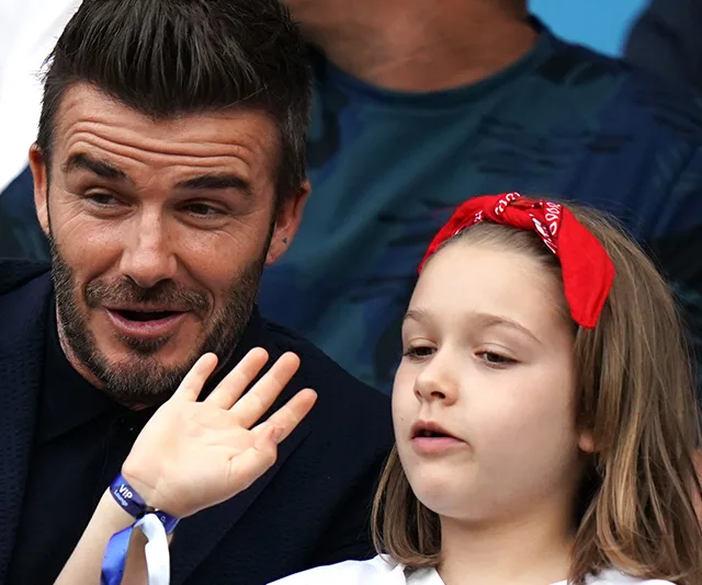 Father and daughter at a soccer game; father smiling, daughter with a red bow, waving.