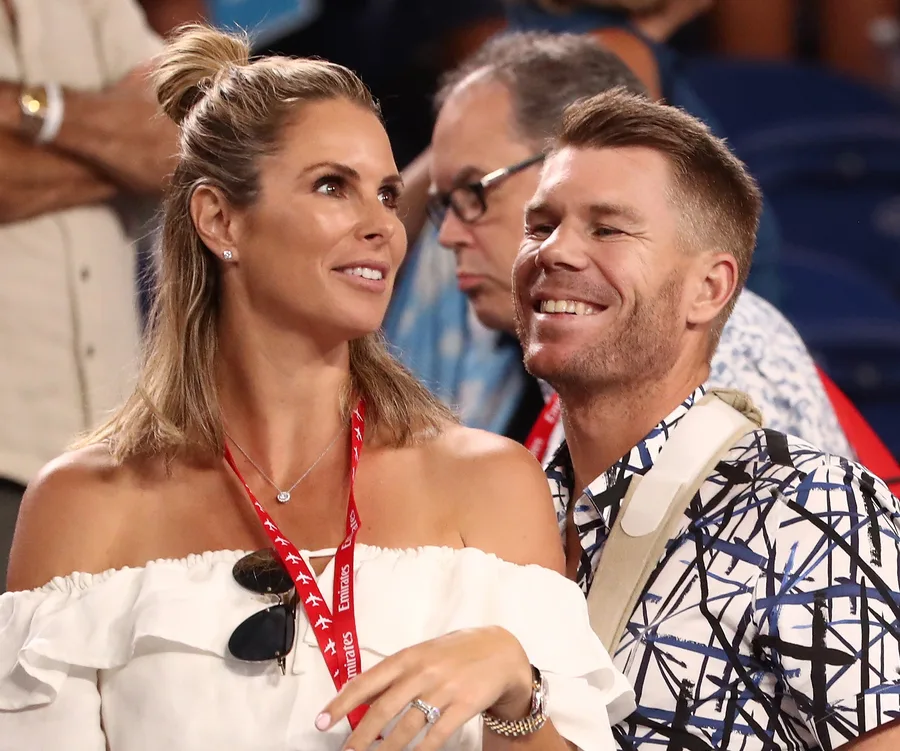 A woman and a man smiling, wearing lanyards at a public event.