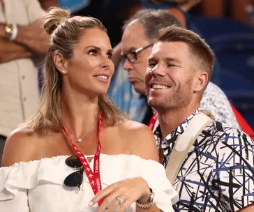 A woman and a man smiling, wearing lanyards at a public event.
