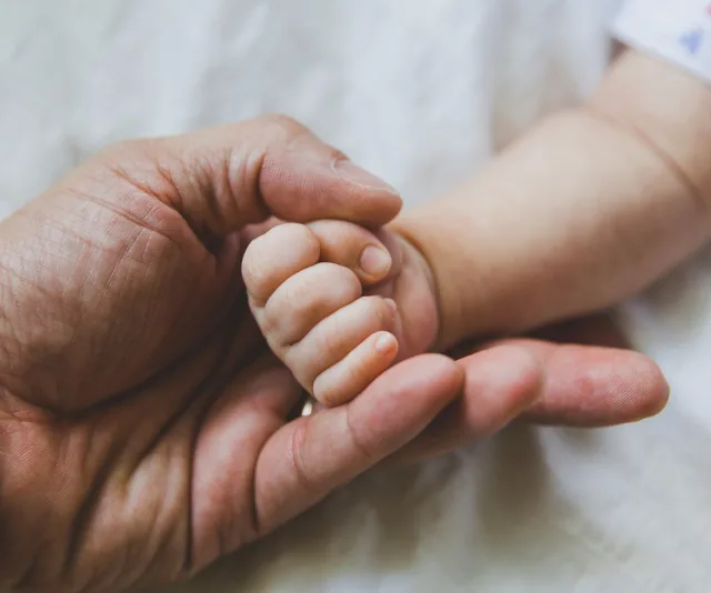 Father holding a baby's hand, symbolizing bonding and care.