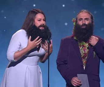 Two presenters on stage at the 2019 Logie Awards, both wearing fake beards, delivering a speech.